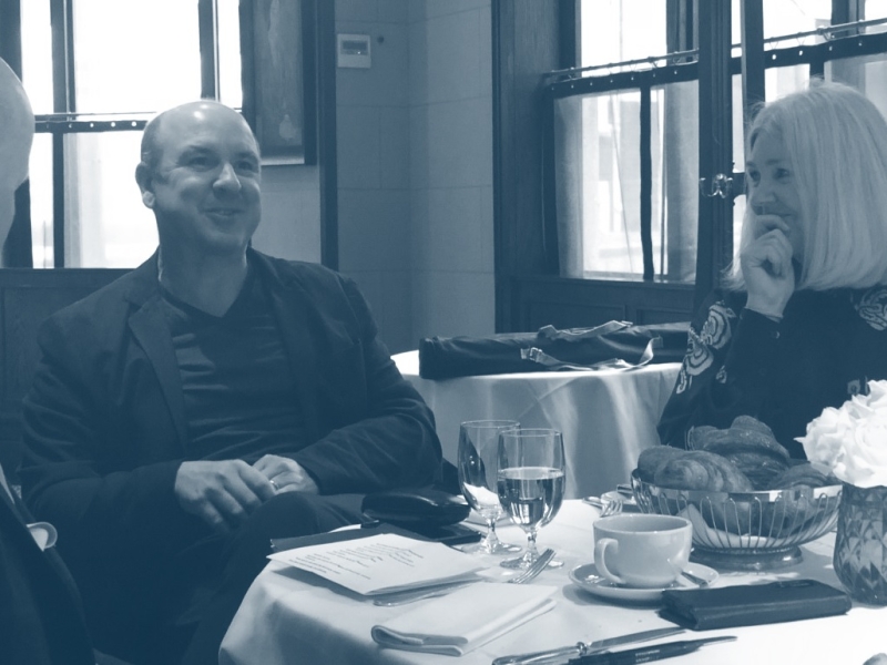 A group of three sitting down talking with a basket of bakery, drinks, paperwork on the table in black and white