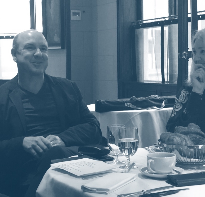 A group of three sitting down talking with a basket of bakery, drinks, paperwork on the table in black and white