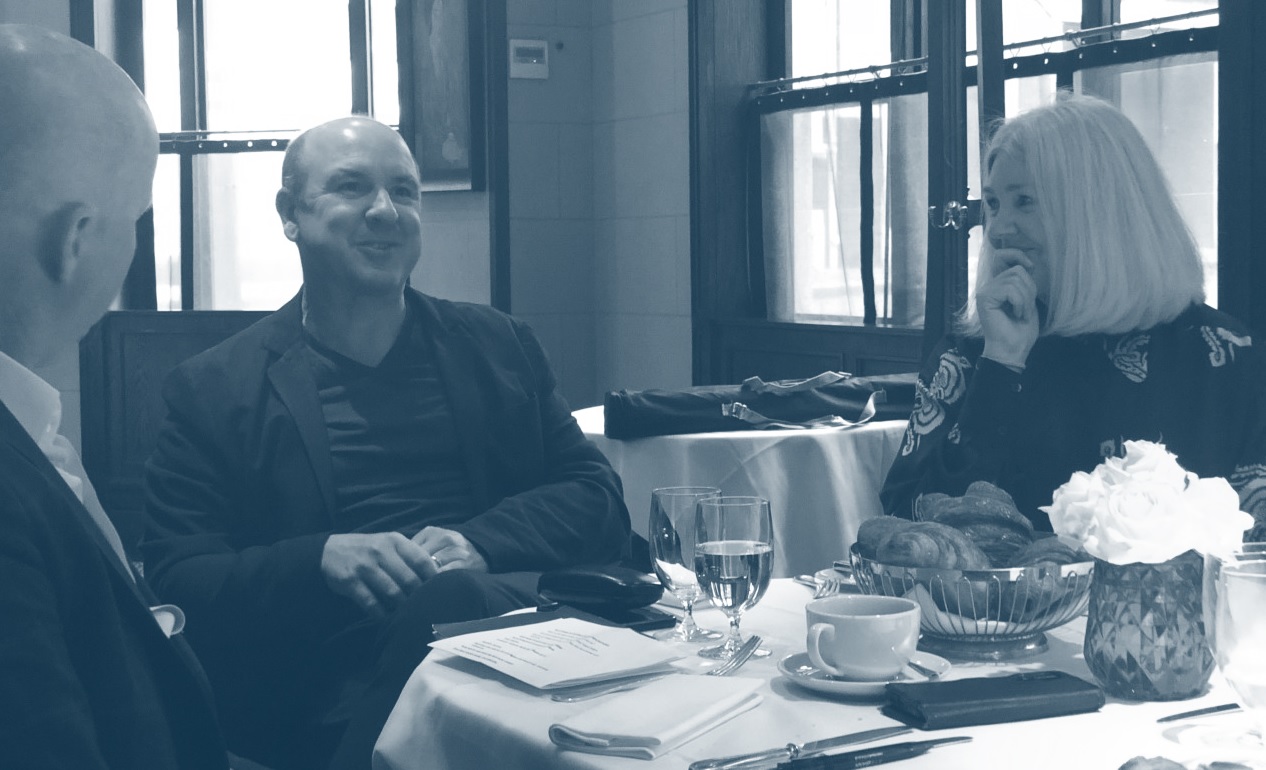 A group of three sitting down talking with a basket of bakery, drinks, paperwork on the table in black and white