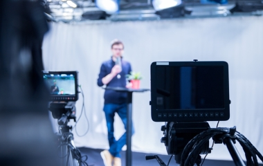 Person standing by a small table in front of cameras