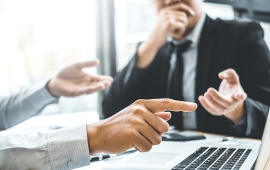 Image of two businessmen having a conversation pointing into a laptop screen
