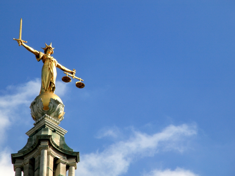 golden statue holding a sword and a scale with a crown on a golden ball with a clear blue sky in the background