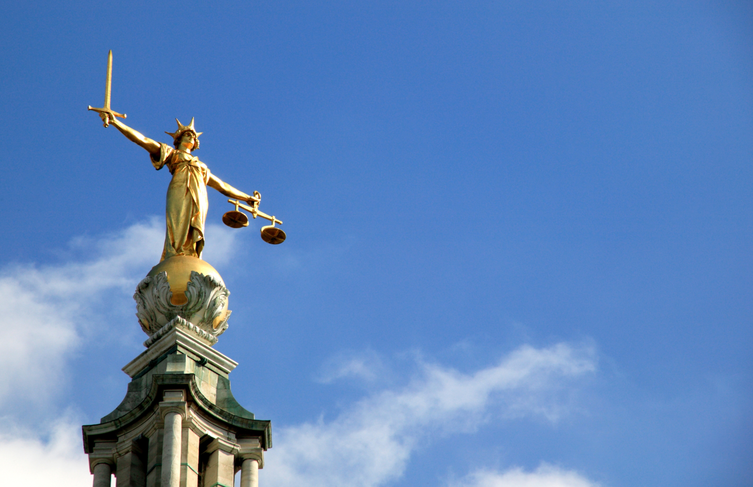 golden statue holding a sword and a scale with a crown on a golden ball with a clear blue sky in the background