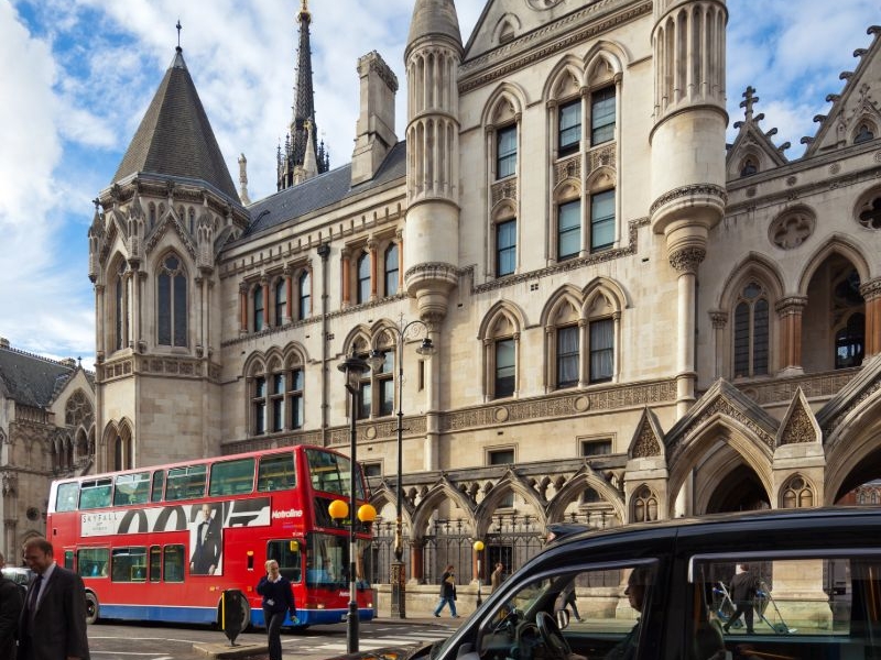 Large beige building with busy streets with red buses and black cab and people crossing the zebra crossing