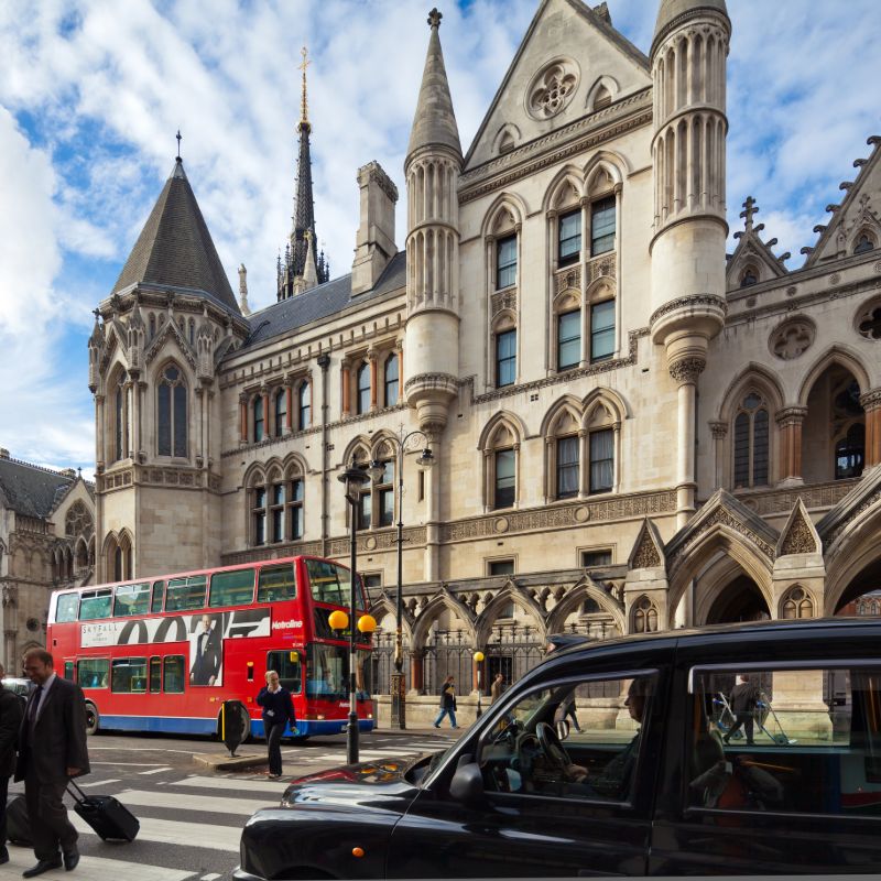 Large beige building with busy streets with red buses and black cab and people crossing the zebra crossing