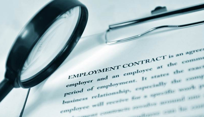 Closeup of employment contract on a clipboard with a magnifying glass up-close