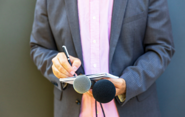 Person holding pen and paper and two microphones
