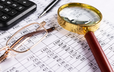 Pair of glasses and magnifying glass with a calculator and paper